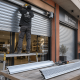Instalador ajusta una persiana metu00e1lica en un local; muestra opciones perforadas y su00f3lidas: Que opciones existen para instalar persianas metalicas en locales comerciales