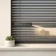 Composición minimalista con persianas metálicas en una ventana; destaca un suculento y la silueta de un edificio en Hospitalet.