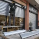 Instalador ajusta una persiana metu00e1lica en un local; muestra opciones perforadas y su00f3lidas: Que opciones existen para instalar persianas metalicas en locales comerciales